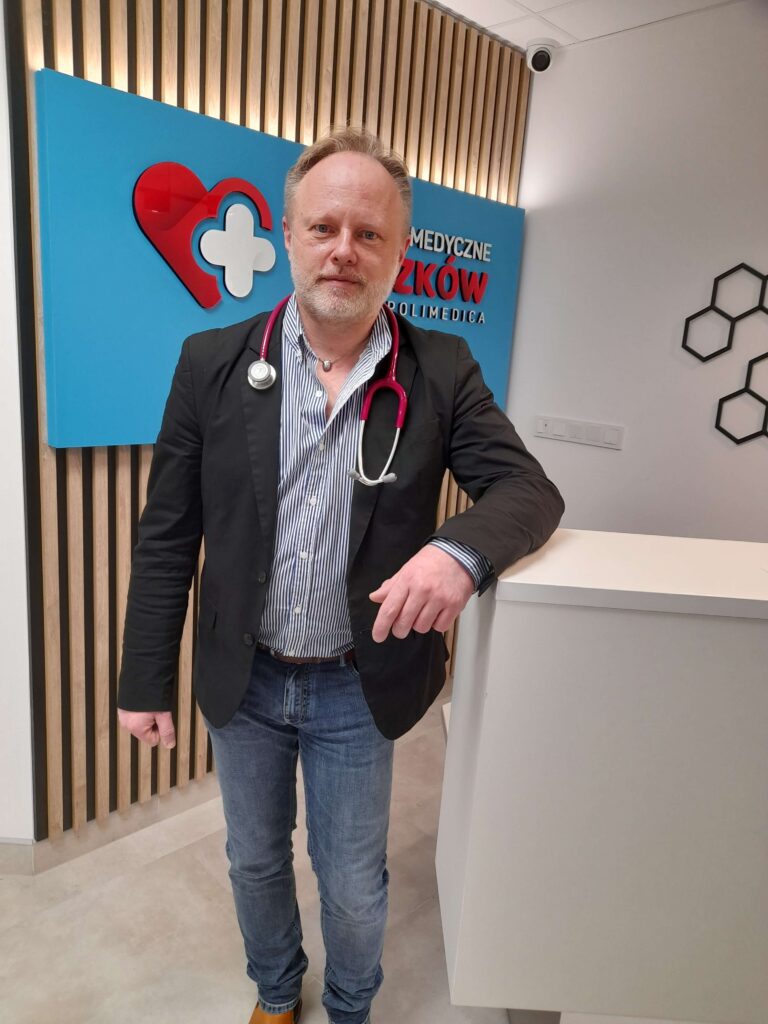 dr Marcin Rzeszutko stoi oparty o ladę rejestracji centrum medycznego Myszków